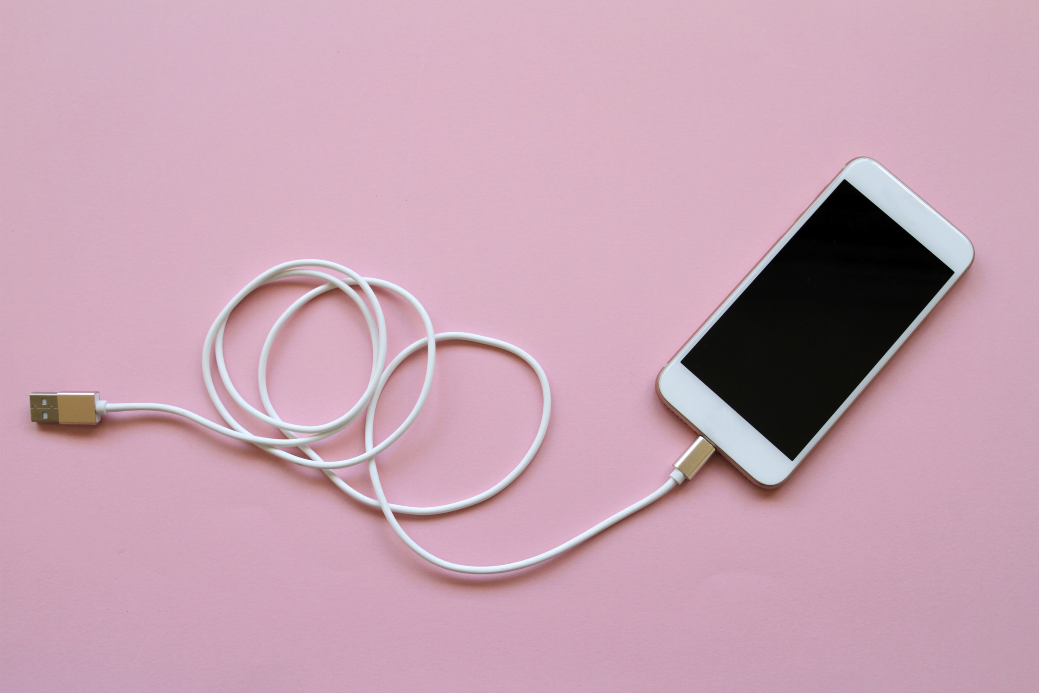 smartphone lying face up on a pink background with a charging cable attached